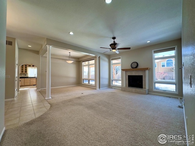 unfurnished living room featuring light colored carpet, a healthy amount of sunlight, and a tiled fireplace