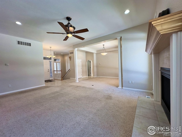 unfurnished living room featuring a tiled fireplace, light colored carpet, and ceiling fan