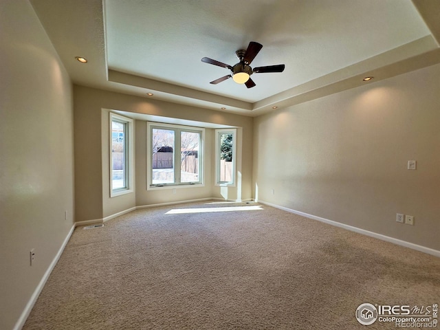 carpeted spare room with a raised ceiling and ceiling fan