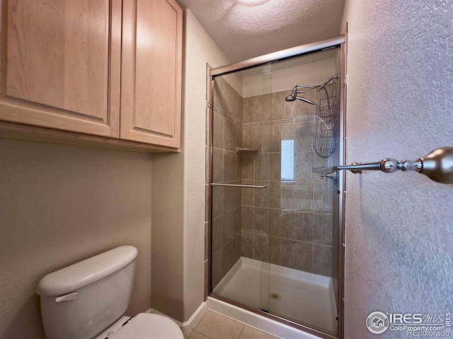 bathroom featuring tile patterned floors, toilet, a shower with door, and a textured ceiling