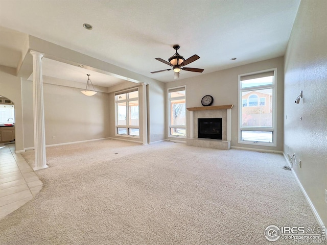 unfurnished living room featuring ornate columns, a healthy amount of sunlight, and light colored carpet