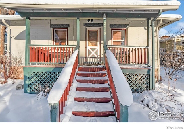 snow covered property entrance with covered porch