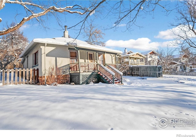 snow covered house with a chimney, fence, and brick siding