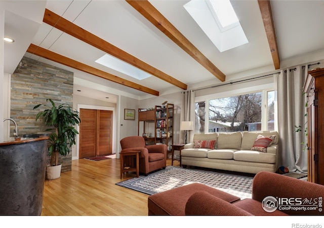 living room featuring sink, vaulted ceiling with skylight, and light hardwood / wood-style flooring