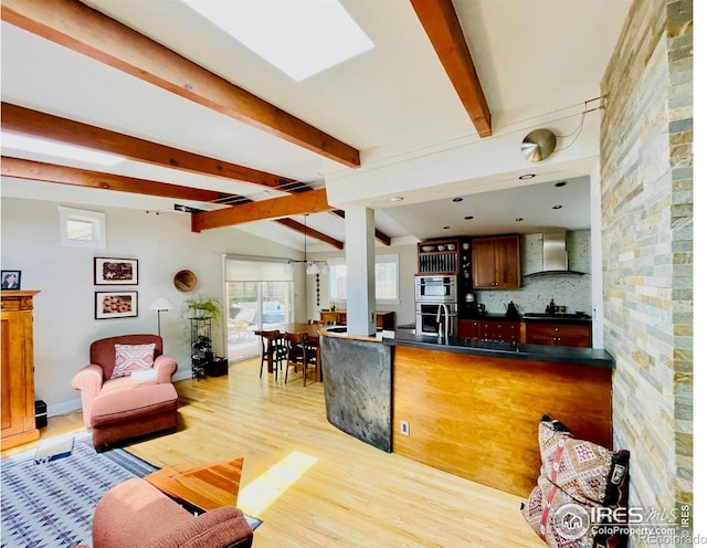 kitchen with wall chimney exhaust hood, vaulted ceiling with beams, light hardwood / wood-style flooring, oven, and black gas stovetop