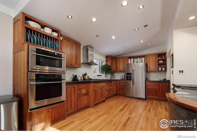 kitchen featuring wall chimney range hood, appliances with stainless steel finishes, decorative backsplash, vaulted ceiling, and light wood-type flooring