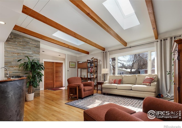 living room with lofted ceiling with skylight, sink, and light hardwood / wood-style flooring