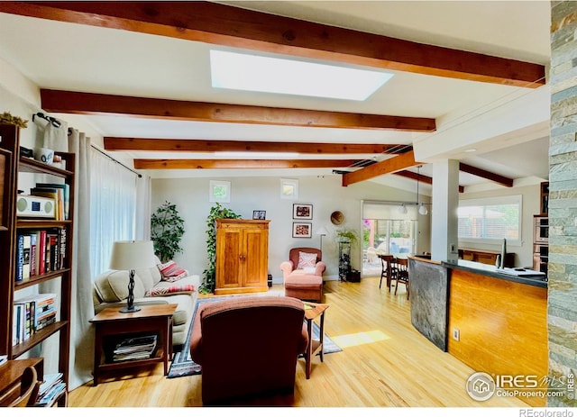 living room with a large fireplace, vaulted ceiling with skylight, and light hardwood / wood-style flooring