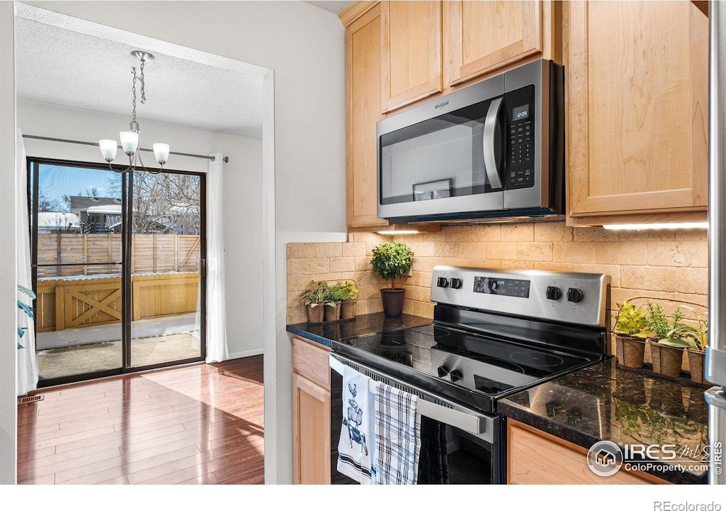 kitchen featuring stainless steel appliances, light brown cabinetry, hardwood / wood-style floors, and hanging light fixtures