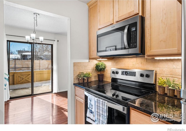 kitchen featuring stainless steel appliances, light brown cabinetry, hardwood / wood-style floors, and hanging light fixtures