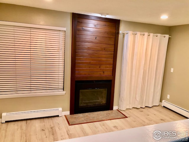 unfurnished living room with baseboard heating, a fireplace, and hardwood / wood-style floors