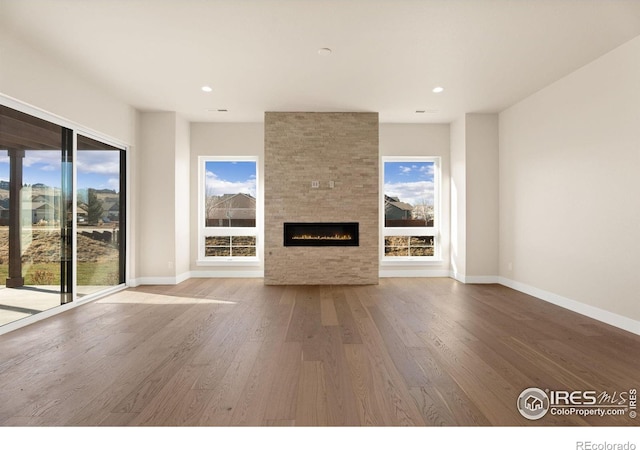 unfurnished living room with hardwood / wood-style floors, a wealth of natural light, and a large fireplace