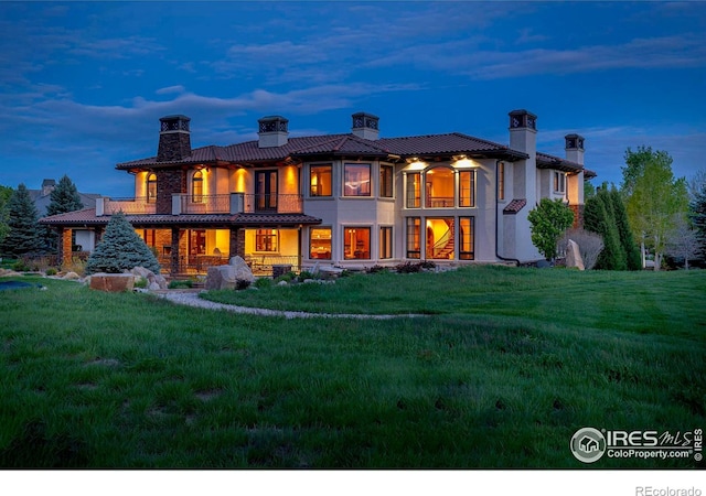 back house at dusk featuring a lawn