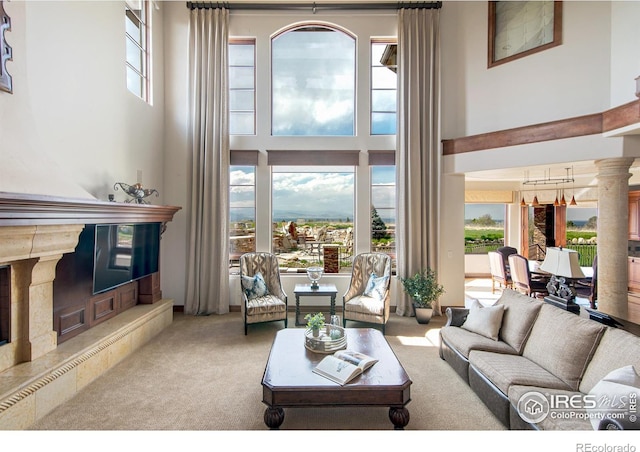 living room with a towering ceiling, light colored carpet, a premium fireplace, and ornate columns