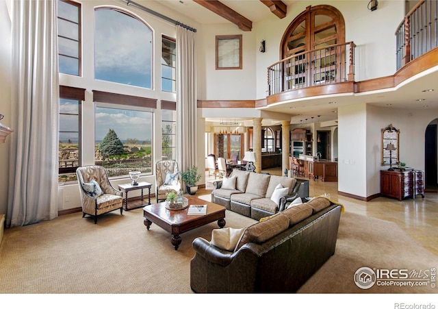 living room with a high ceiling, plenty of natural light, decorative columns, and beamed ceiling