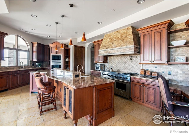 kitchen featuring premium range hood, decorative light fixtures, decorative backsplash, stainless steel appliances, and a center island with sink