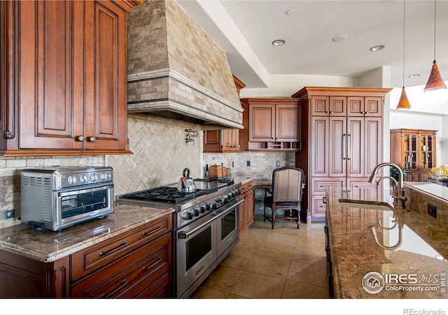 kitchen with sink, decorative light fixtures, custom range hood, stone counters, and range with two ovens