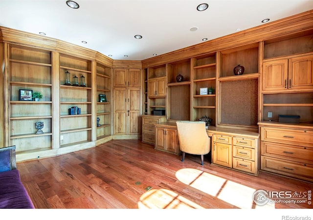 unfurnished office featuring wood-type flooring, built in desk, and built in shelves