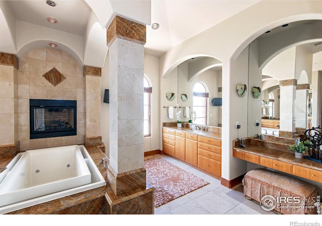 bathroom featuring tile patterned floors, vanity, a tiled fireplace, and tiled tub