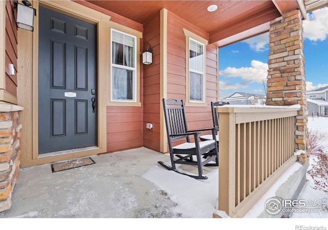 snow covered property entrance with covered porch