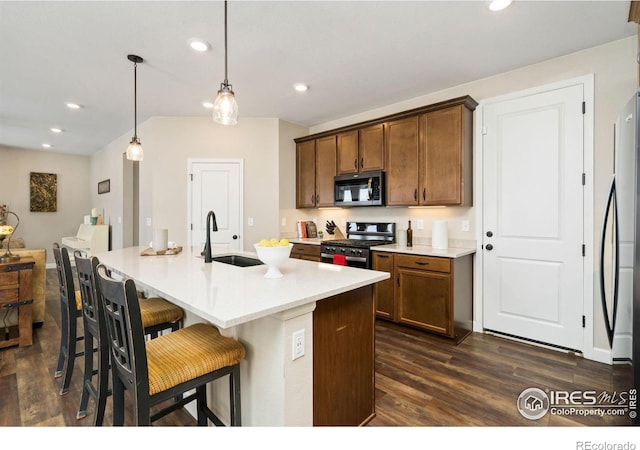 kitchen with sink, decorative light fixtures, dark hardwood / wood-style flooring, stainless steel appliances, and a kitchen island with sink