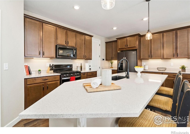 kitchen featuring a breakfast bar area, hanging light fixtures, an island with sink, hardwood / wood-style flooring, and stainless steel appliances