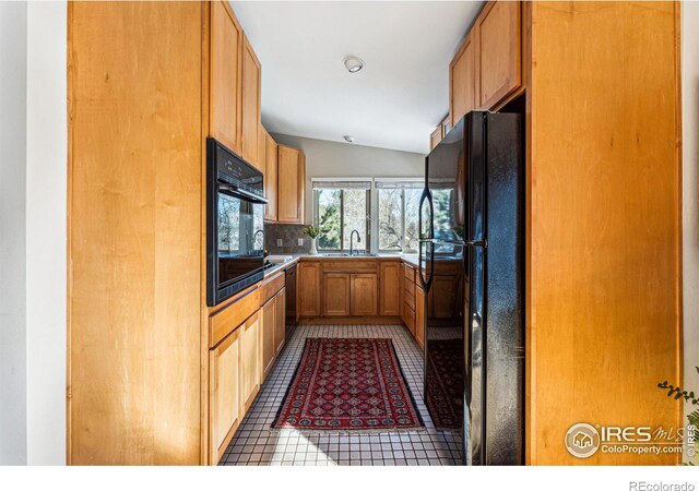 kitchen featuring tasteful backsplash, lofted ceiling, sink, tile patterned flooring, and black appliances