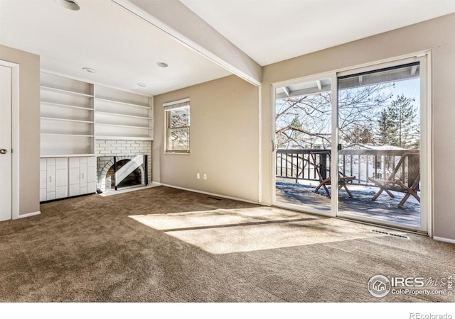 unfurnished living room featuring built in shelves, a fireplace, carpet floors, and a wealth of natural light