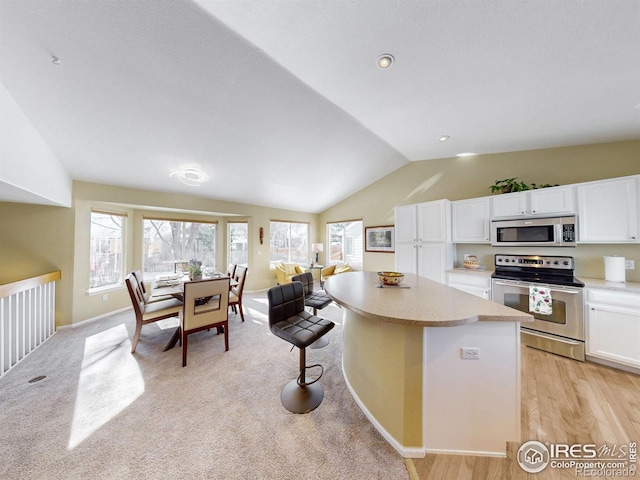 kitchen with stainless steel appliances, white cabinetry, a kitchen island, and vaulted ceiling