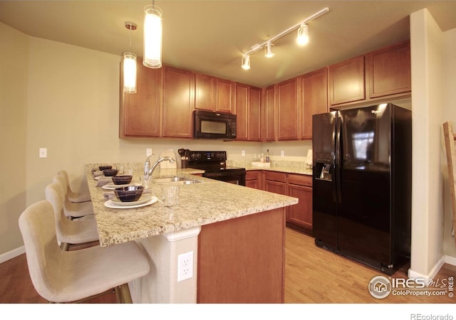 kitchen with a breakfast bar, pendant lighting, black appliances, sink, and kitchen peninsula