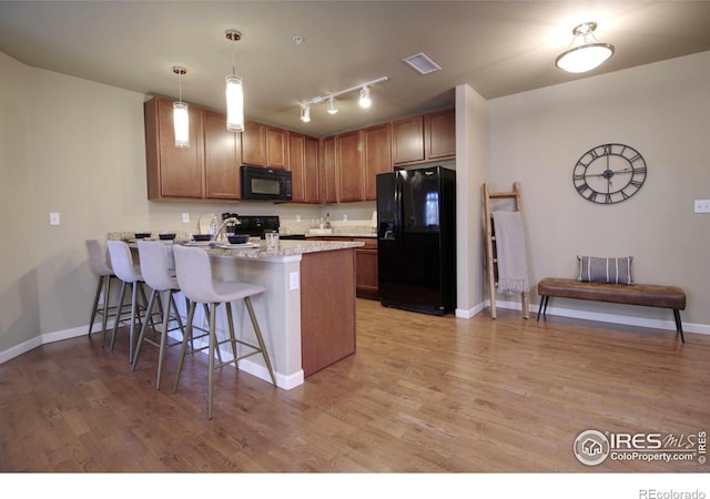 kitchen featuring decorative light fixtures, black appliances, a kitchen breakfast bar, kitchen peninsula, and light hardwood / wood-style flooring