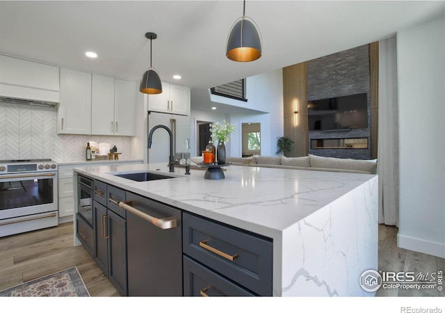 kitchen with sink, appliances with stainless steel finishes, hanging light fixtures, white cabinets, and a center island with sink