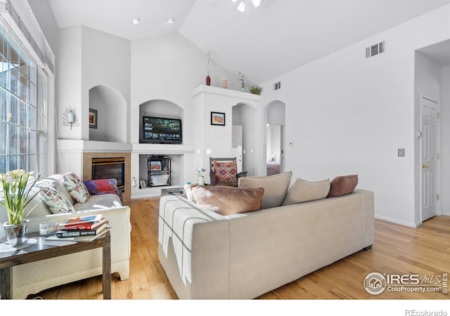 living room featuring a tile fireplace, light hardwood / wood-style floors, and a high ceiling