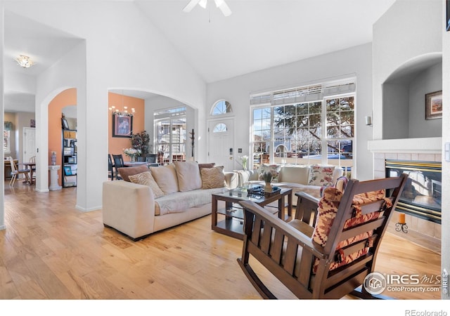 living room featuring high vaulted ceiling, ceiling fan with notable chandelier, a fireplace, and light hardwood / wood-style floors