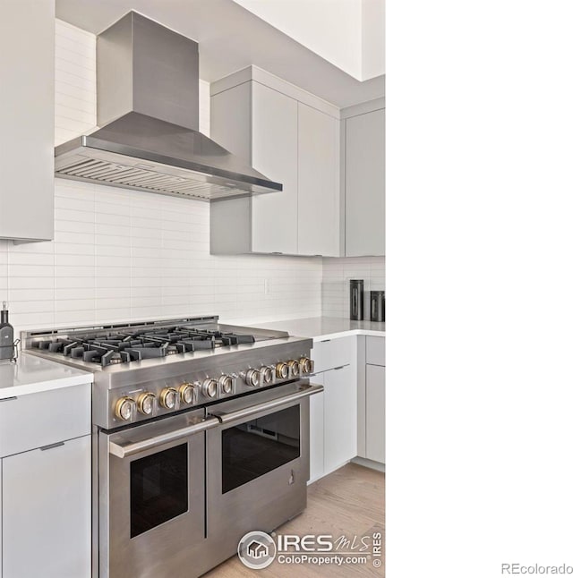 kitchen featuring backsplash, double oven range, light hardwood / wood-style floors, and wall chimney range hood