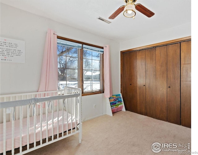 bedroom featuring a crib, carpet flooring, ceiling fan, and a closet