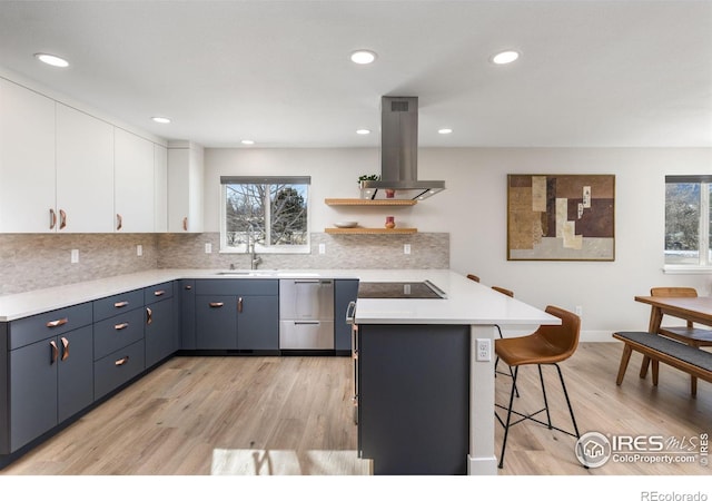 kitchen featuring island range hood, a breakfast bar, white cabinets, light countertops, and open shelves