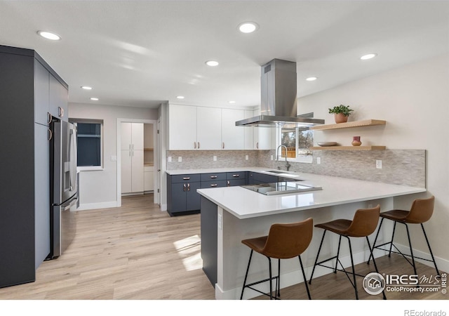 kitchen with a peninsula, light countertops, stainless steel refrigerator with ice dispenser, a kitchen bar, and open shelves