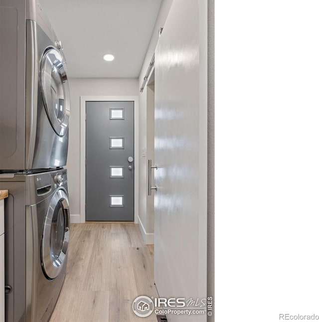 washroom featuring laundry area, a barn door, baseboards, light wood-style flooring, and stacked washing maching and dryer