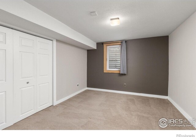 finished below grade area featuring a textured ceiling, baseboards, and light colored carpet