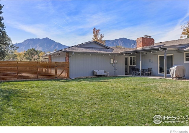 rear view of house with fence, a mountain view, a patio, and a yard