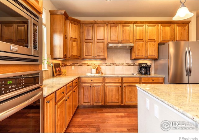 kitchen featuring pendant lighting, wood-type flooring, decorative backsplash, light stone counters, and stainless steel appliances