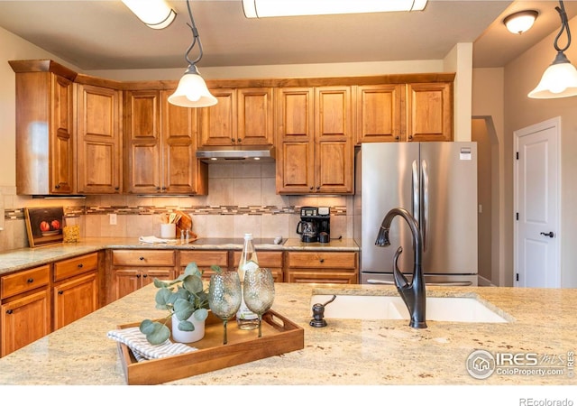 kitchen with decorative light fixtures, stainless steel refrigerator, black electric cooktop, light stone countertops, and backsplash