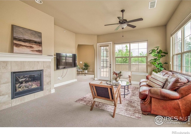 living room with ceiling fan, a tiled fireplace, and light carpet