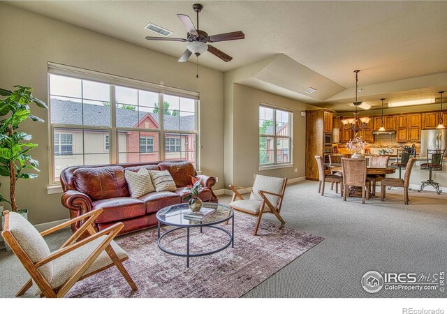 carpeted living room with ceiling fan with notable chandelier and vaulted ceiling