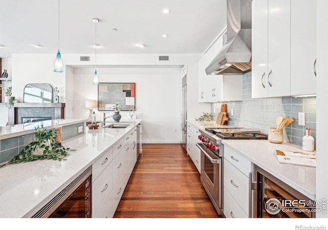 kitchen with stainless steel appliances, white cabinetry, hanging light fixtures, and wall chimney exhaust hood