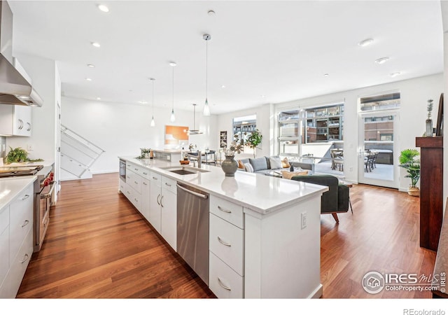 kitchen featuring appliances with stainless steel finishes, white cabinetry, sink, hanging light fixtures, and a center island with sink