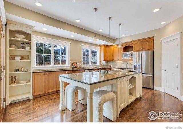 kitchen featuring a kitchen island with sink, dark stone countertops, stainless steel appliances, a kitchen breakfast bar, and decorative light fixtures