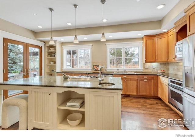 kitchen with sink, hanging light fixtures, a center island with sink, appliances with stainless steel finishes, and dark stone counters