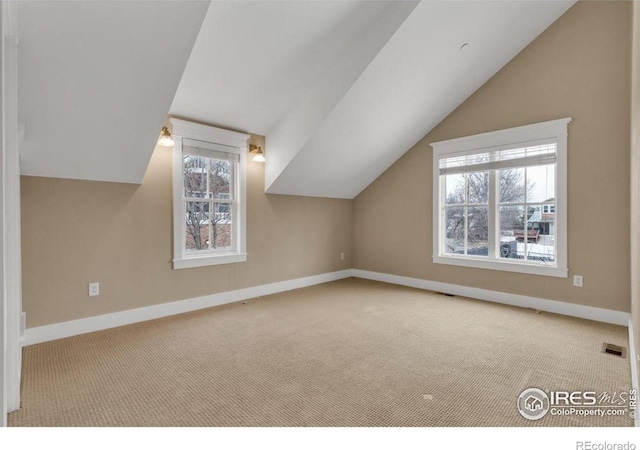 additional living space featuring light colored carpet, a healthy amount of sunlight, and vaulted ceiling